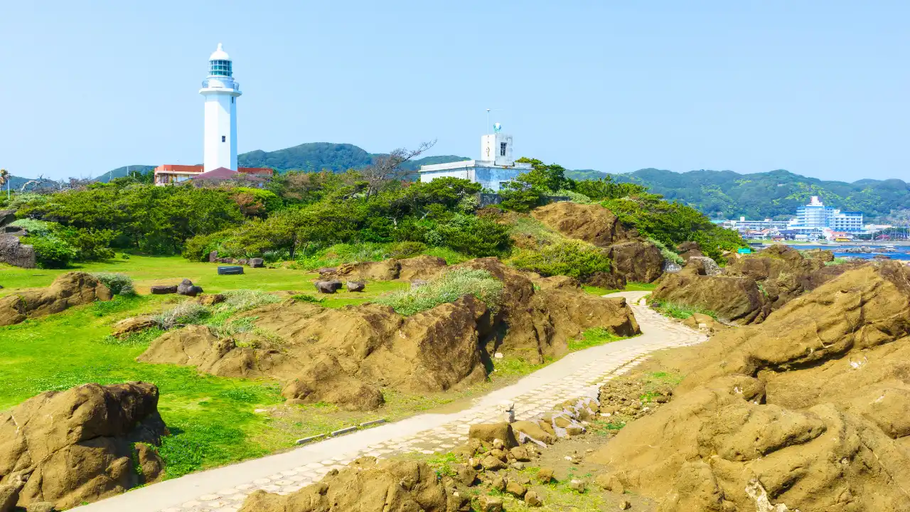 青空と岩場が広がる景色の中に野島崎灯台がみえる風景の画像