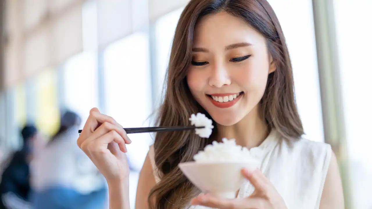 女性がご飯茶碗と箸をもち微笑んでお米を食べようとしている画像