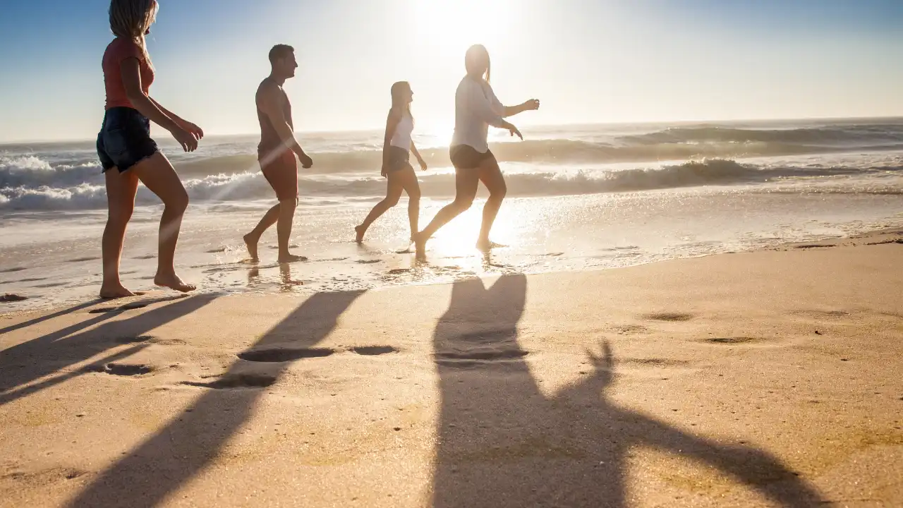 夕方の夕日がさす海を背景に砂浜を男女4人が楽しそうに走っている画像