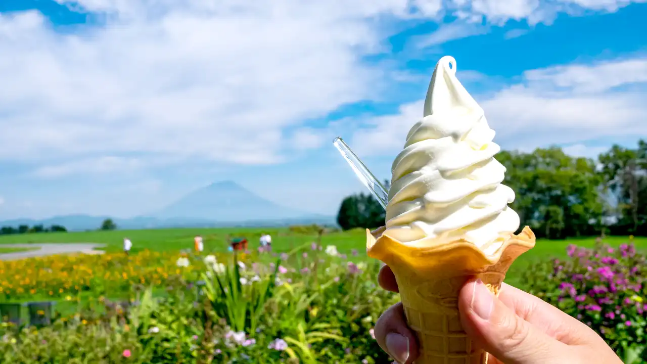 青空が広がり草むらが広がる自然の背景。手前にソフトクリームが写る画像